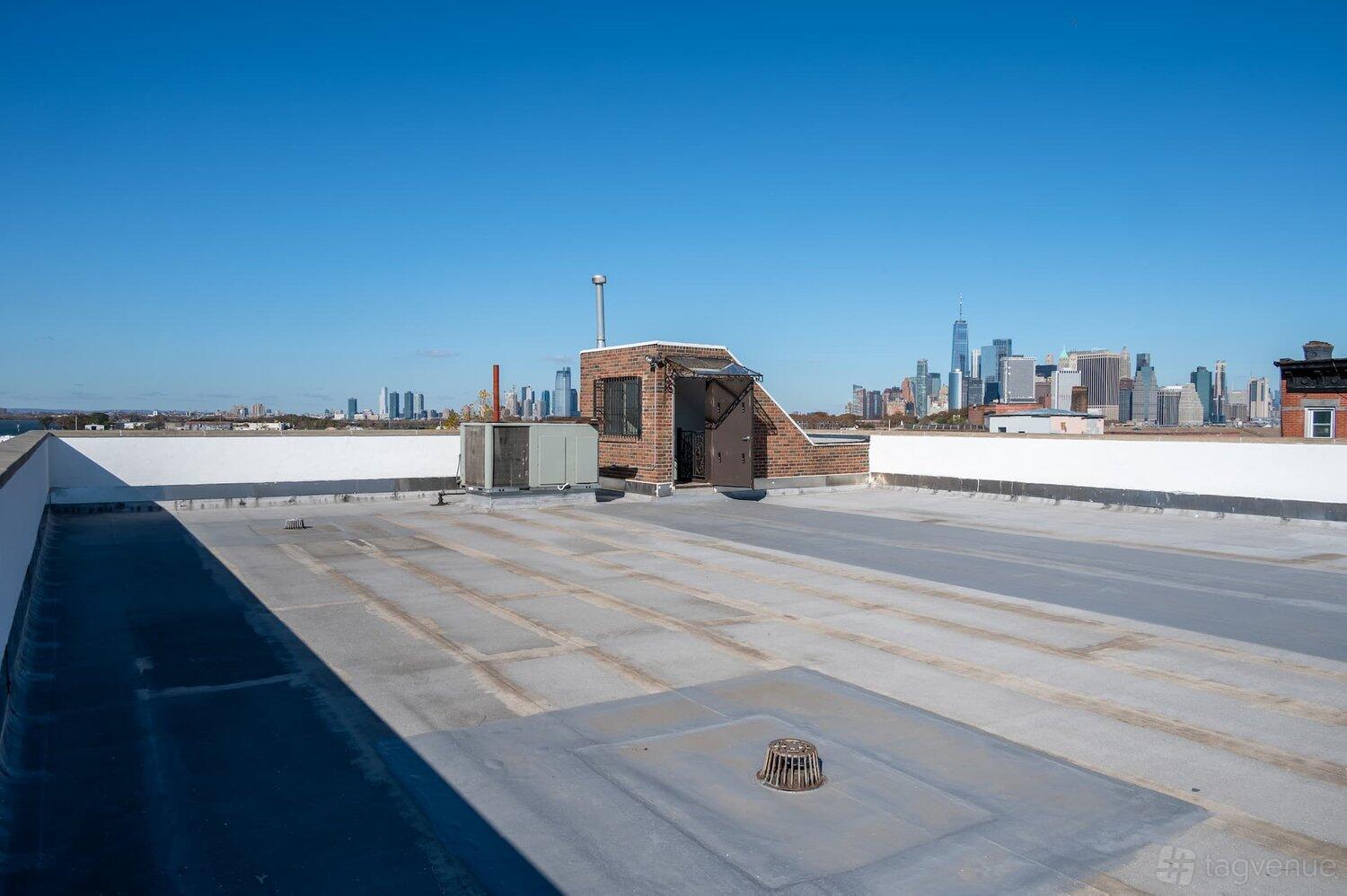 A rooftop area with city skyline views and a small brick access structure at Hook Studios - Dikeman Street.