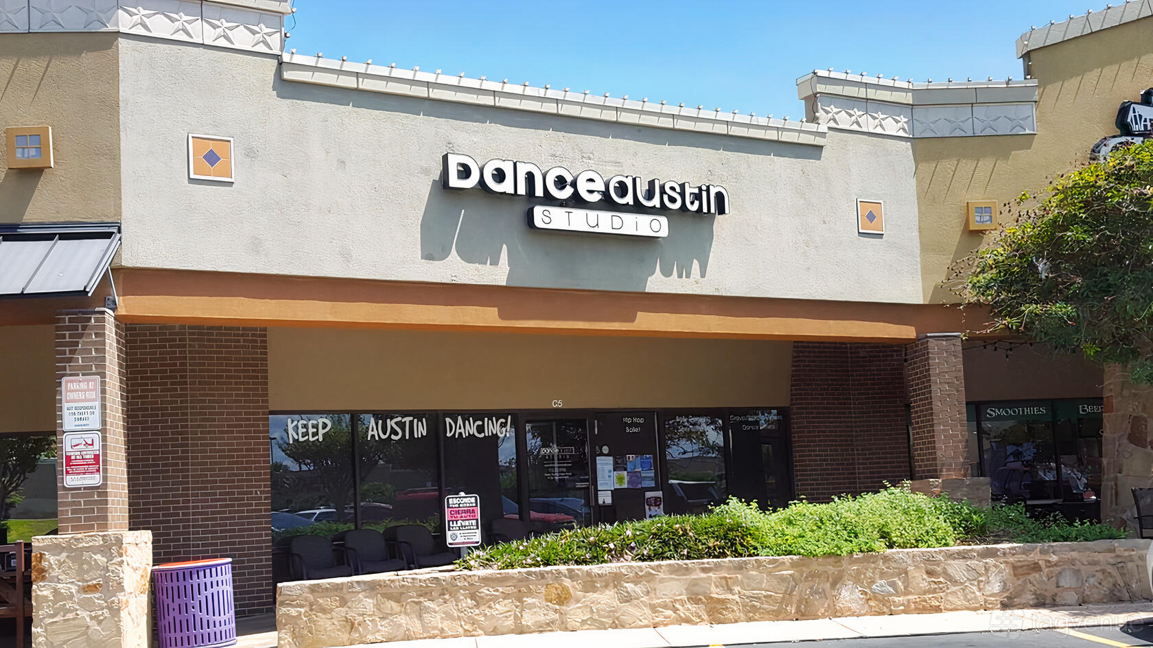 A dance studio with a prominent sign above glass doors in a shopping plaza at Dance Austin Studio.