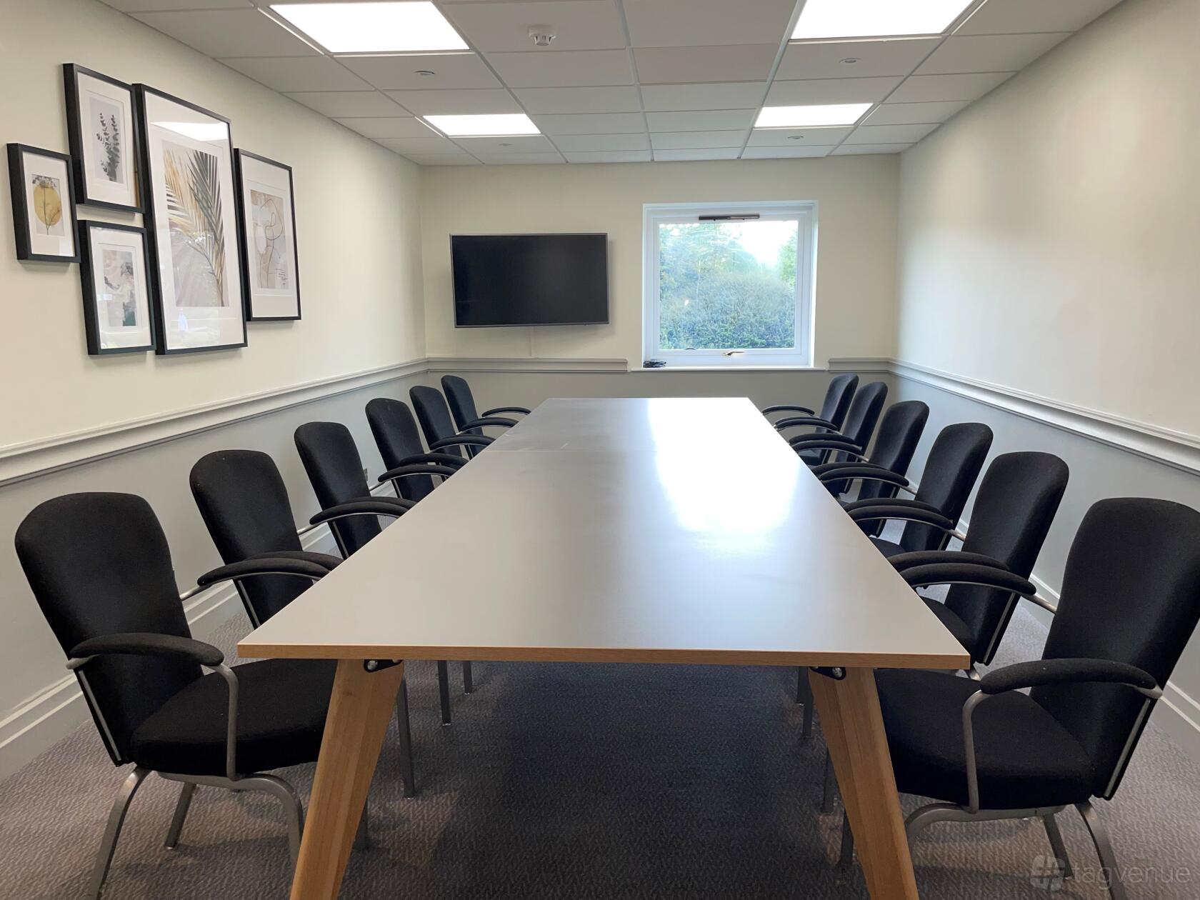 A hotel boardroom with a long conference table, black chairs, wall-mounted screen, and framed artwork at Delta Hotels by Marriott Milton Keynes.