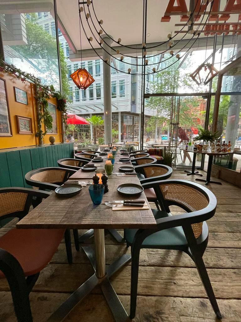 An event space in a restaurant with floor-to-ceiling windows, wooden tables, and woven chairs at Cabana @ St Giles.