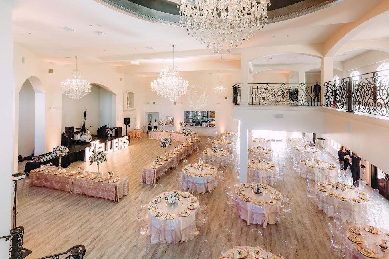 A grand event venue with chandeliers, balcony seating, and round tables with blush linens at Knotting Hill Place.