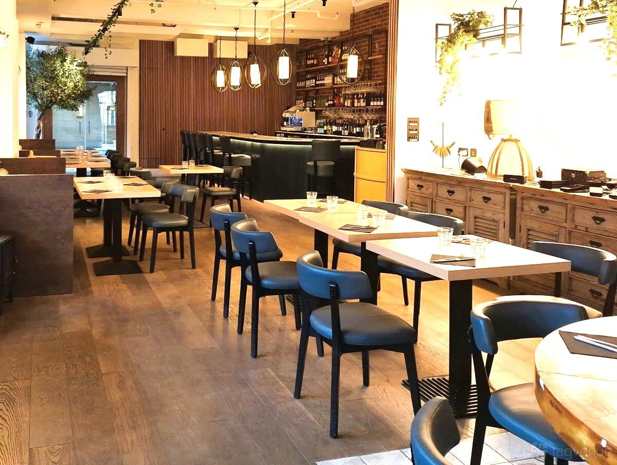 A bar in a restaurant featuring wooden floors, blue chairs, pendant lighting, and a stocked bar at Strings Restaurant.