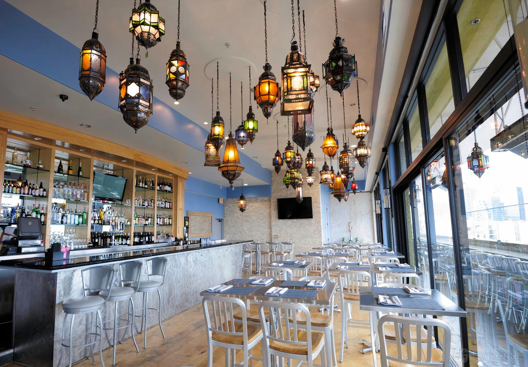 A restaurant with colorful Moroccan-style lanterns, floor-to-ceiling windows, and metal bar stools at Porto Vista Hotel & Suites.