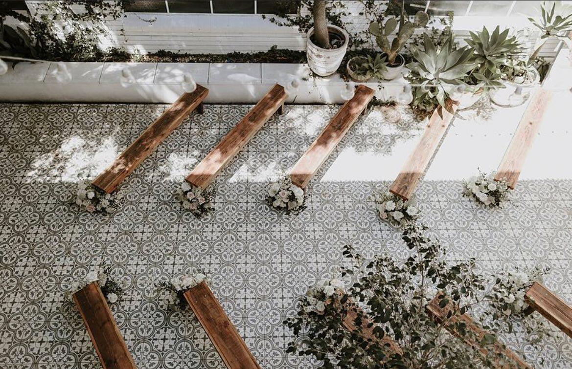 An event venue with patterned tile flooring, wooden benches, and potted greenery at La Porte Space.