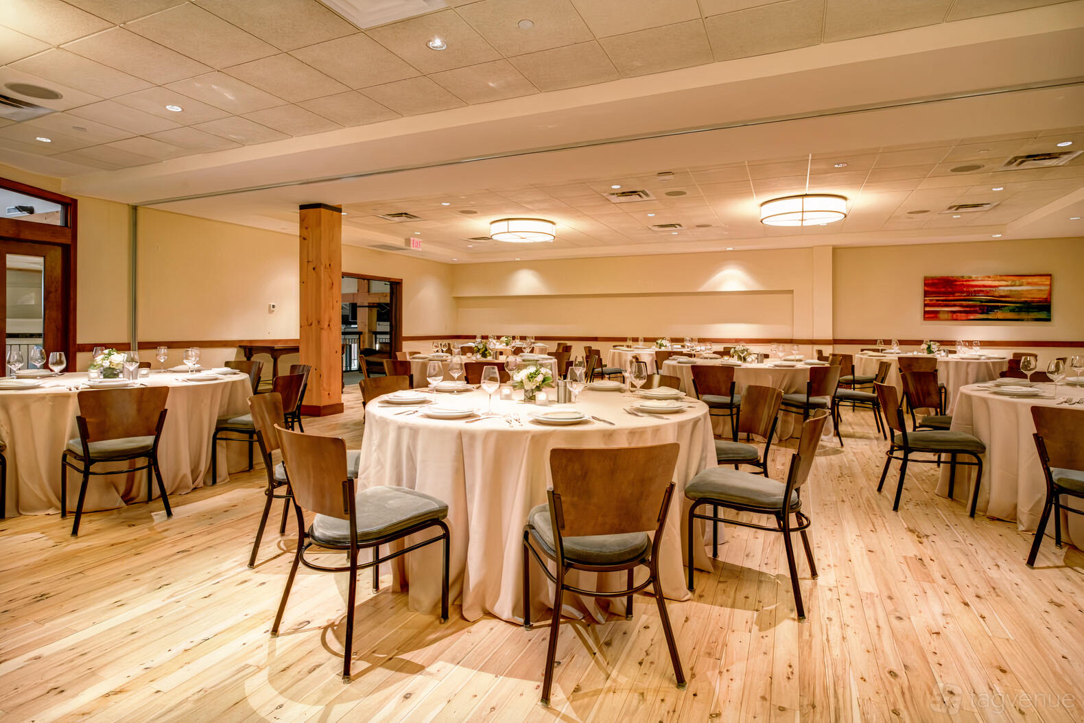 A ballroom with round tables draped in beige linens, wooden floors, and modern ceiling lights at Pinstripes - South Barrington.
