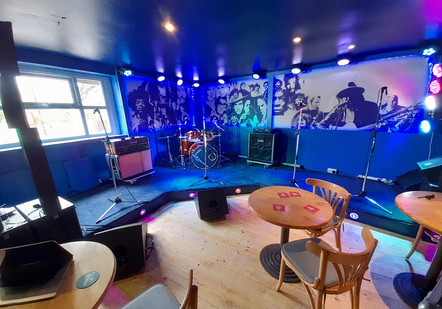 An event venue with a small stage, drum kit, microphones, and music-themed mural at The Tower of Song.