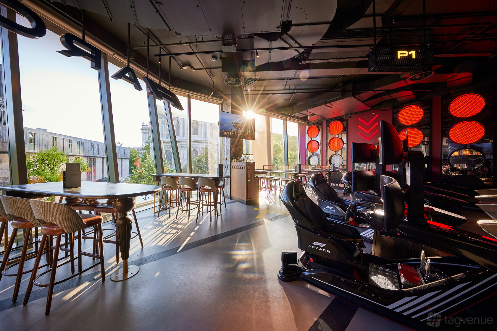A cocktail bar with floor-to-ceiling windows, round tables with stools, and F1 simulators at F1 Arcade, St Pauls, London.