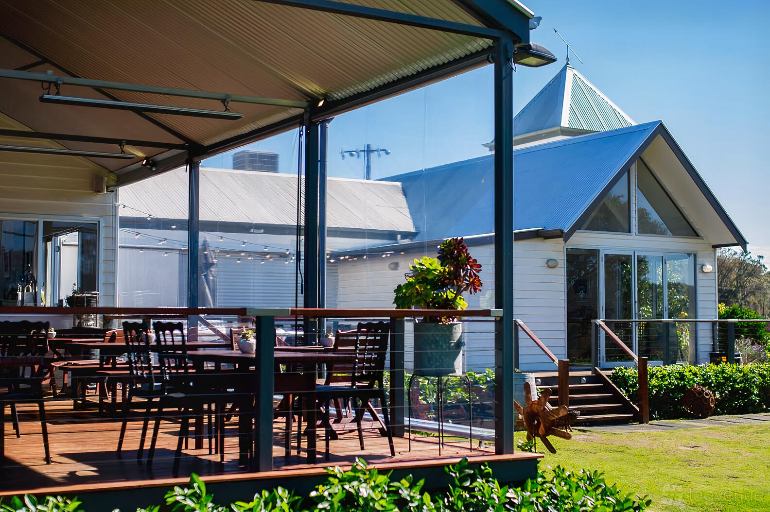 An outdoor restaurant patio with wooden tables, black chairs, and glass railing at Rustico At Hay Shed Hill.