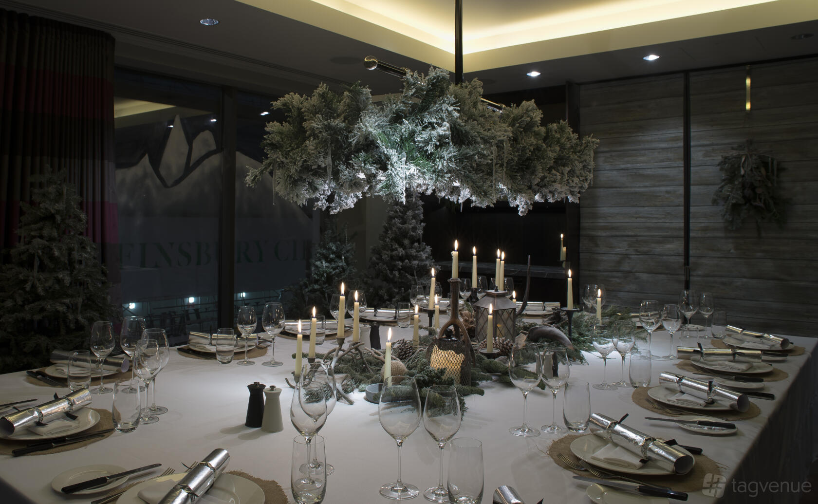 A dining room with a large round table, festive candle centerpiece, and greenery chandelier at South Place Hotel.