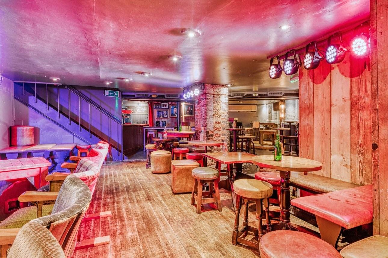 A pub function room with wooden floors, exposed brick columns, round tables, and colorful stage lighting at Kings Head Crouch End.