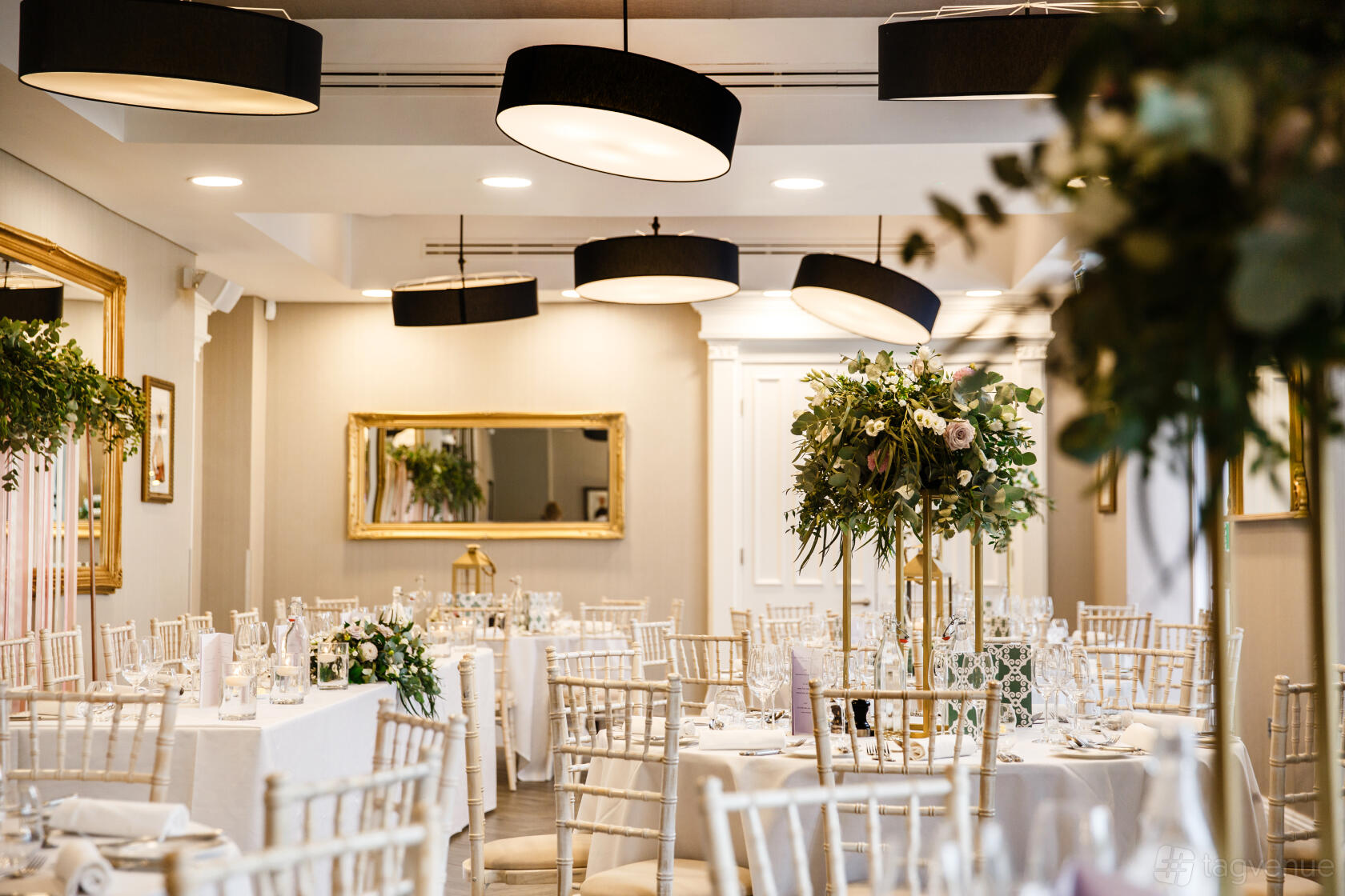 A hotel dining room with round tables, white linens, tall floral centerpieces, and modern black pendant lights at Oddfellows On The Park.