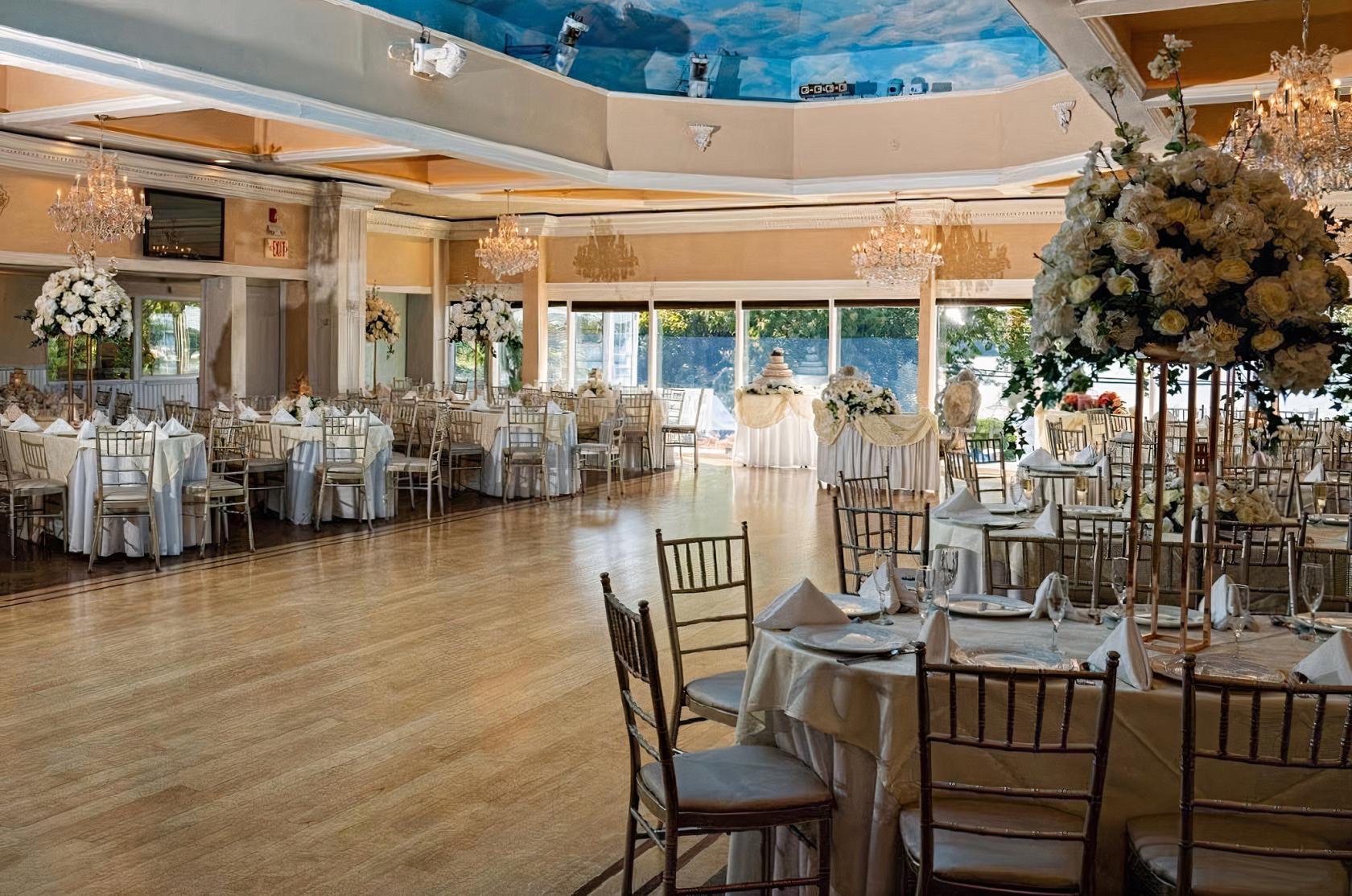An event venue with a spacious ballroom, hardwood floors, chandeliers, and floor-to-ceiling windows at Windows On The Lake.
