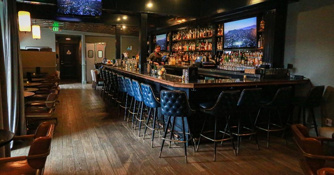 A bar with tufted leather stools, a long polished counter, and shelves of liquor bottles at Georgia's Lounge.