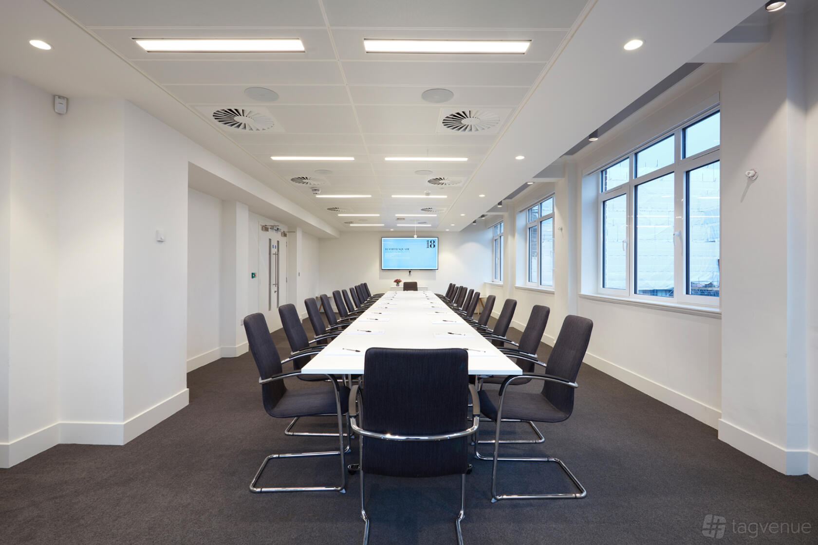 A meeting room with a long rectangular table, black chairs, and large windows at 18 Smith Square.