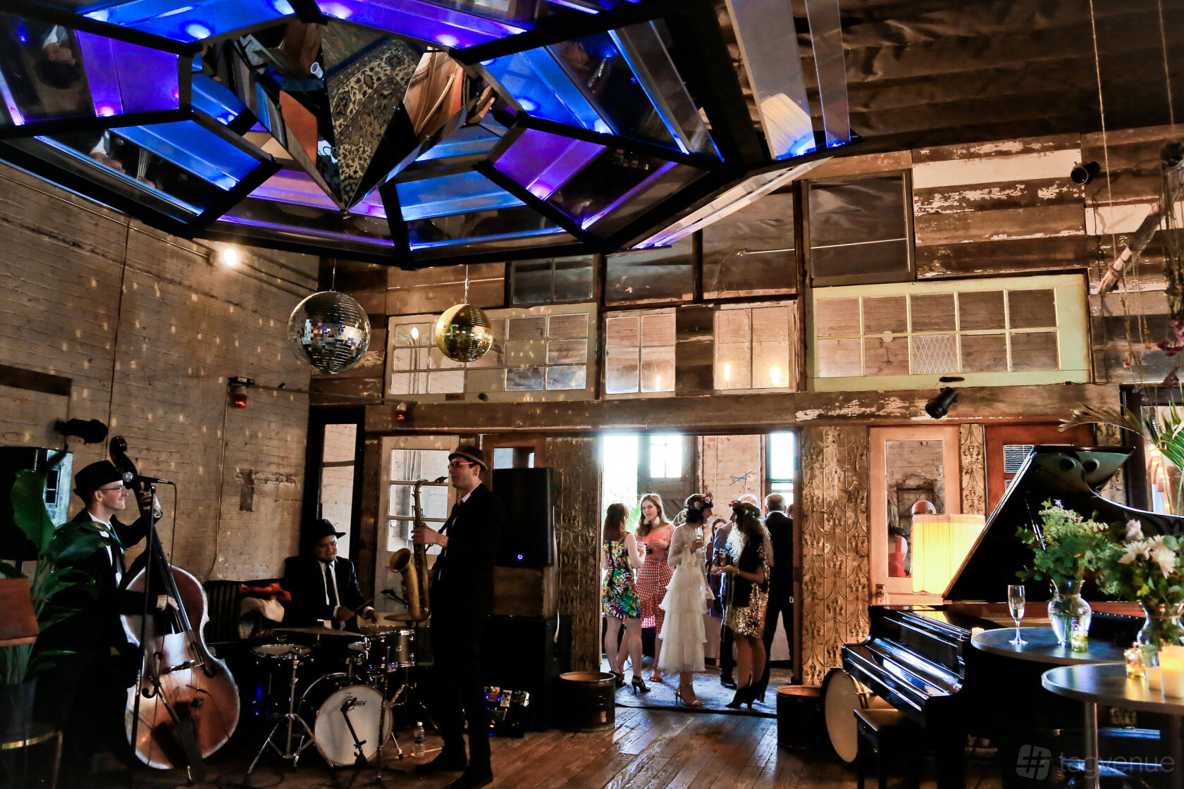 An event venue with exposed brick walls, wooden floors, and a geometric stained-glass ceiling at 5th House Studios.