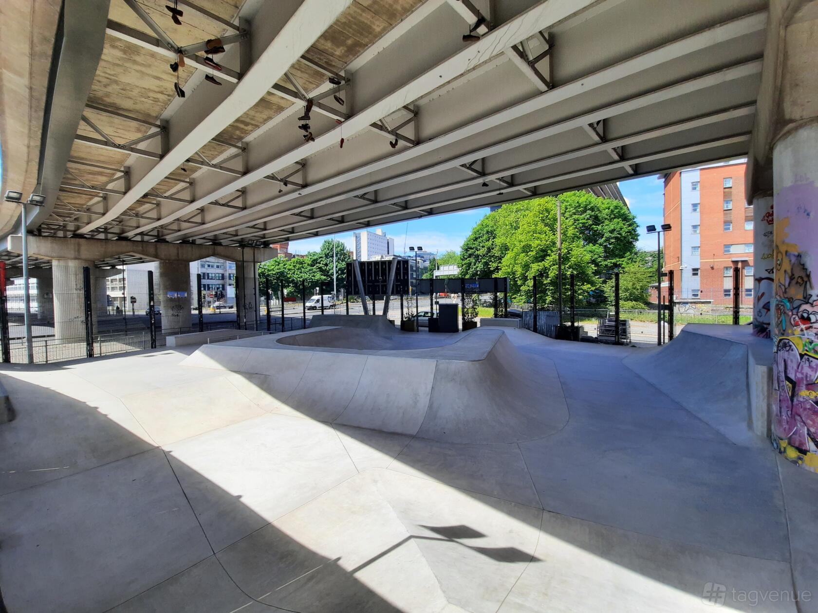 An outdoor skatepark with concrete ramps and graffiti walls under a highway at Projekts Skatepark.