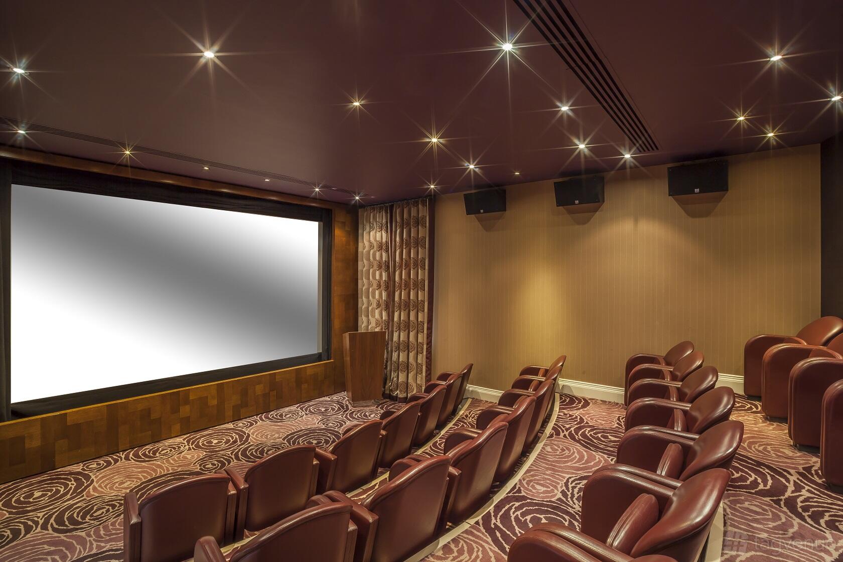 A cinema with plush red theater seats, patterned carpet, and a large projection screen at The Roseate Reading.
