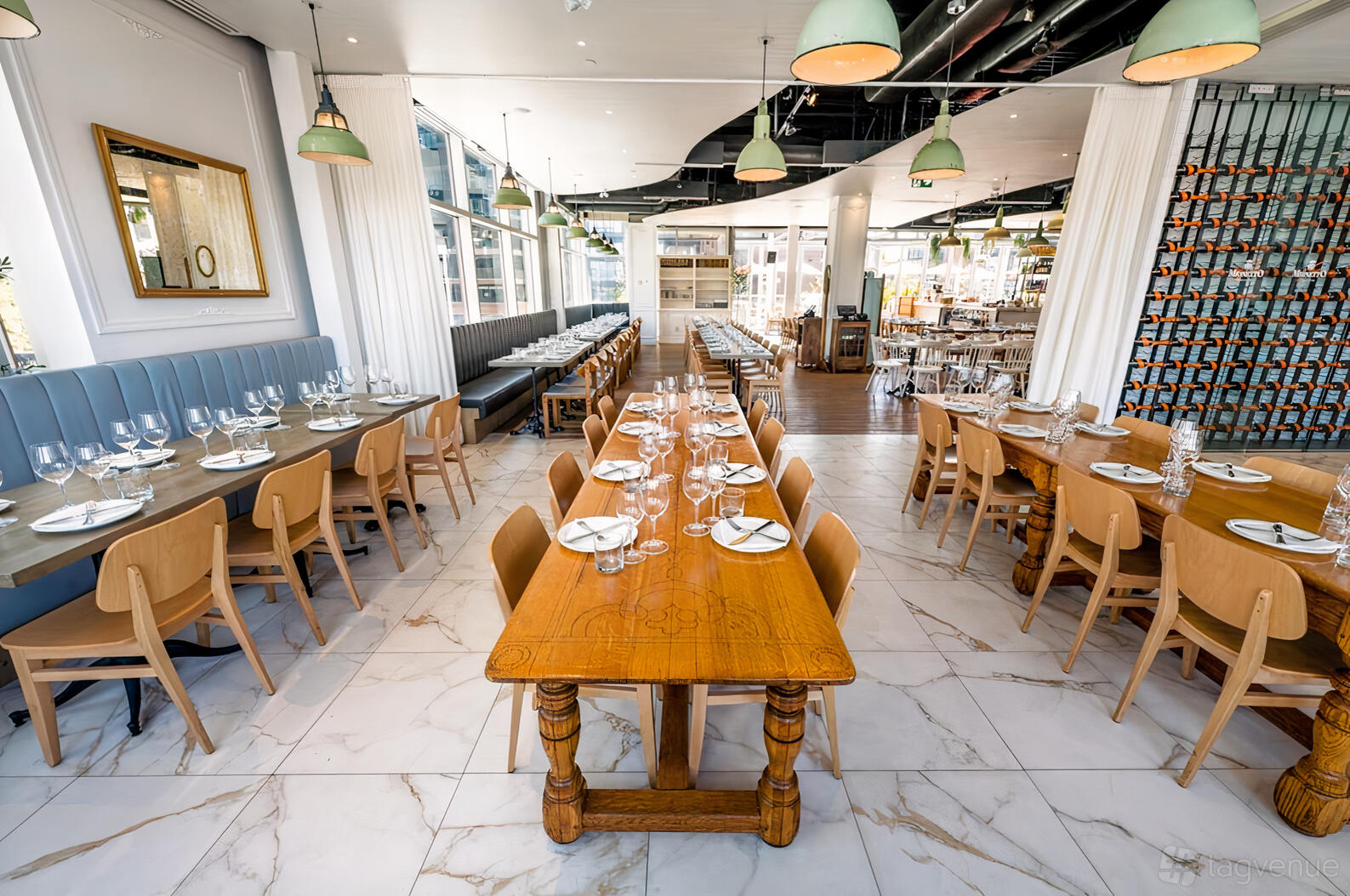 A restaurant with long wooden tables, light wooden chairs, marble tile flooring, and pendant lighting at Nodo Liberty.
