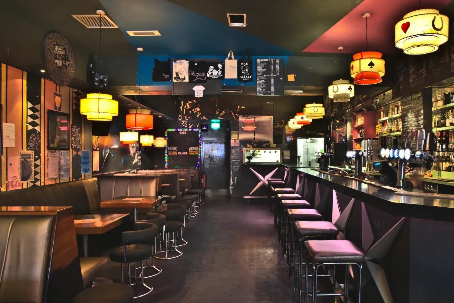 A bar with booth seating, eclectic wall art, colorful pendant lights, and a long bar counter at Nice N Sleazy.