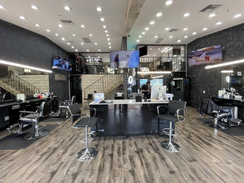 An event venue with salon chairs, wood flooring, and large wall-mounted TVs at Entourage Barbershop.