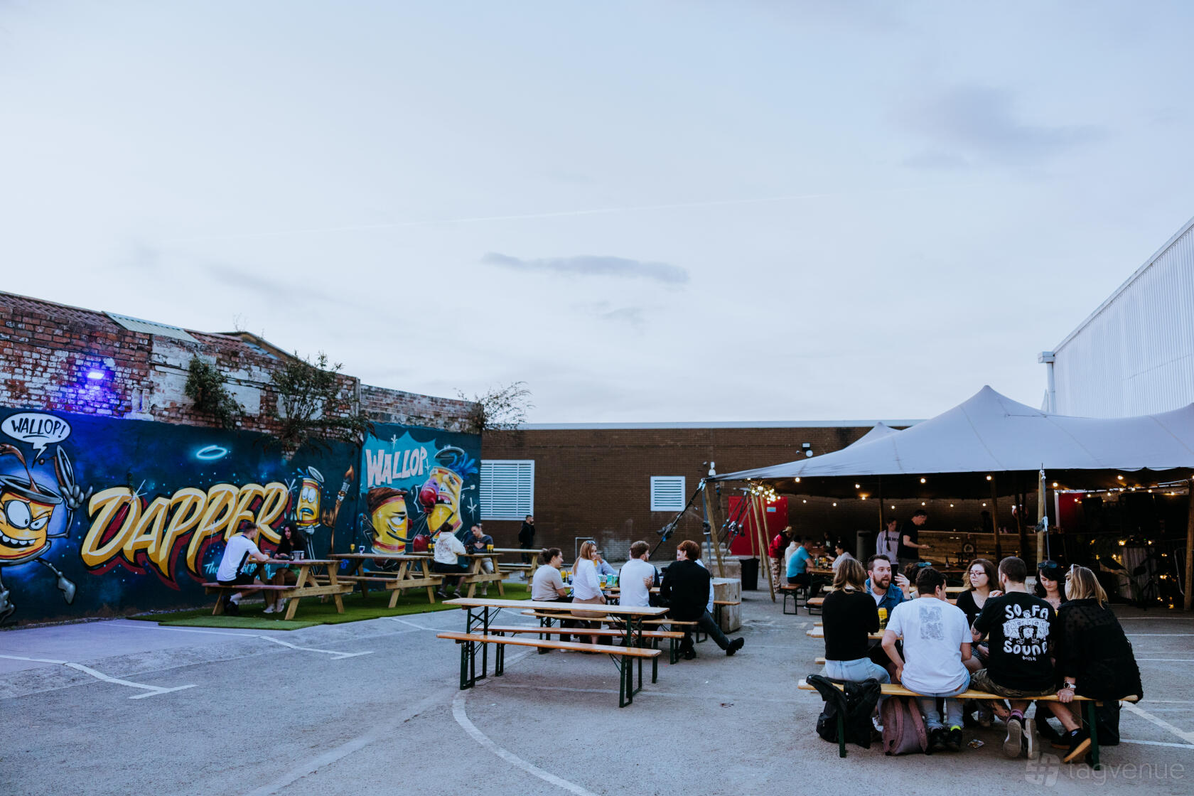 An outdoor event space with picnic tables, wall murals, and a large canopy tent at DOCUMENT.