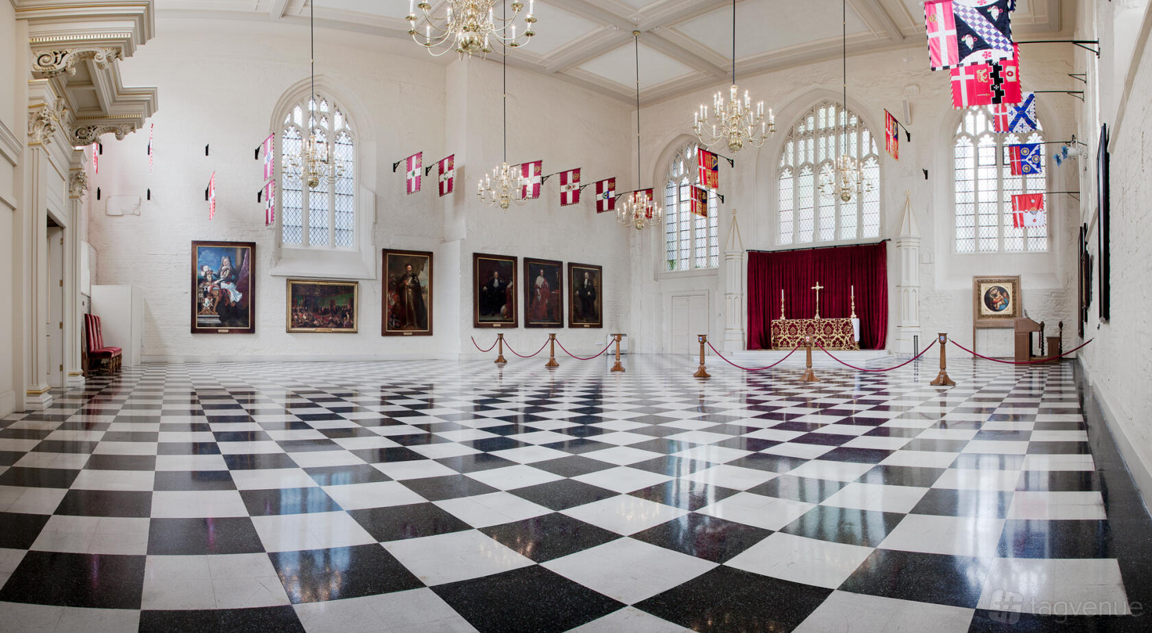An event space in a museum with checkered flooring, arched windows, chandeliers, and historic paintings at Museum of the Order of St John.