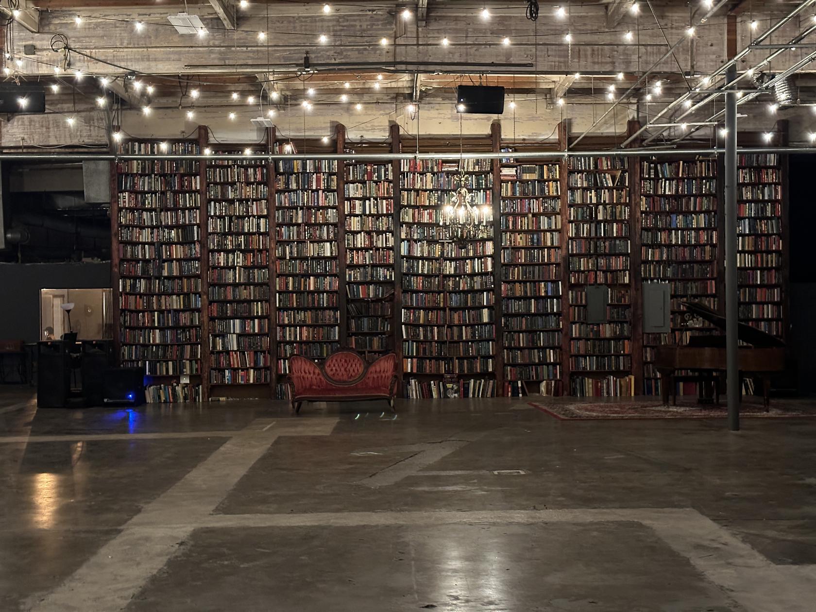 A film studio with a tall wall of bookshelves, a red vintage sofa, and string lights at DTLA Studio.