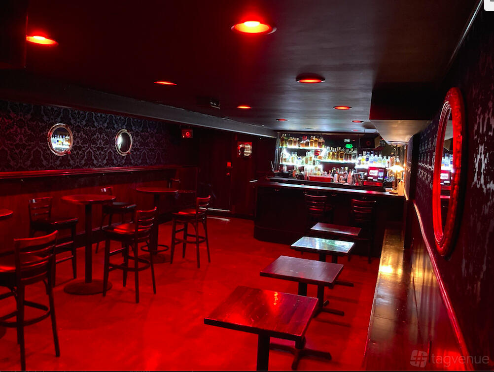 A bar with red ambient lighting, round mirrors on dark patterned walls, and a stocked counter at Columbus Cafe.