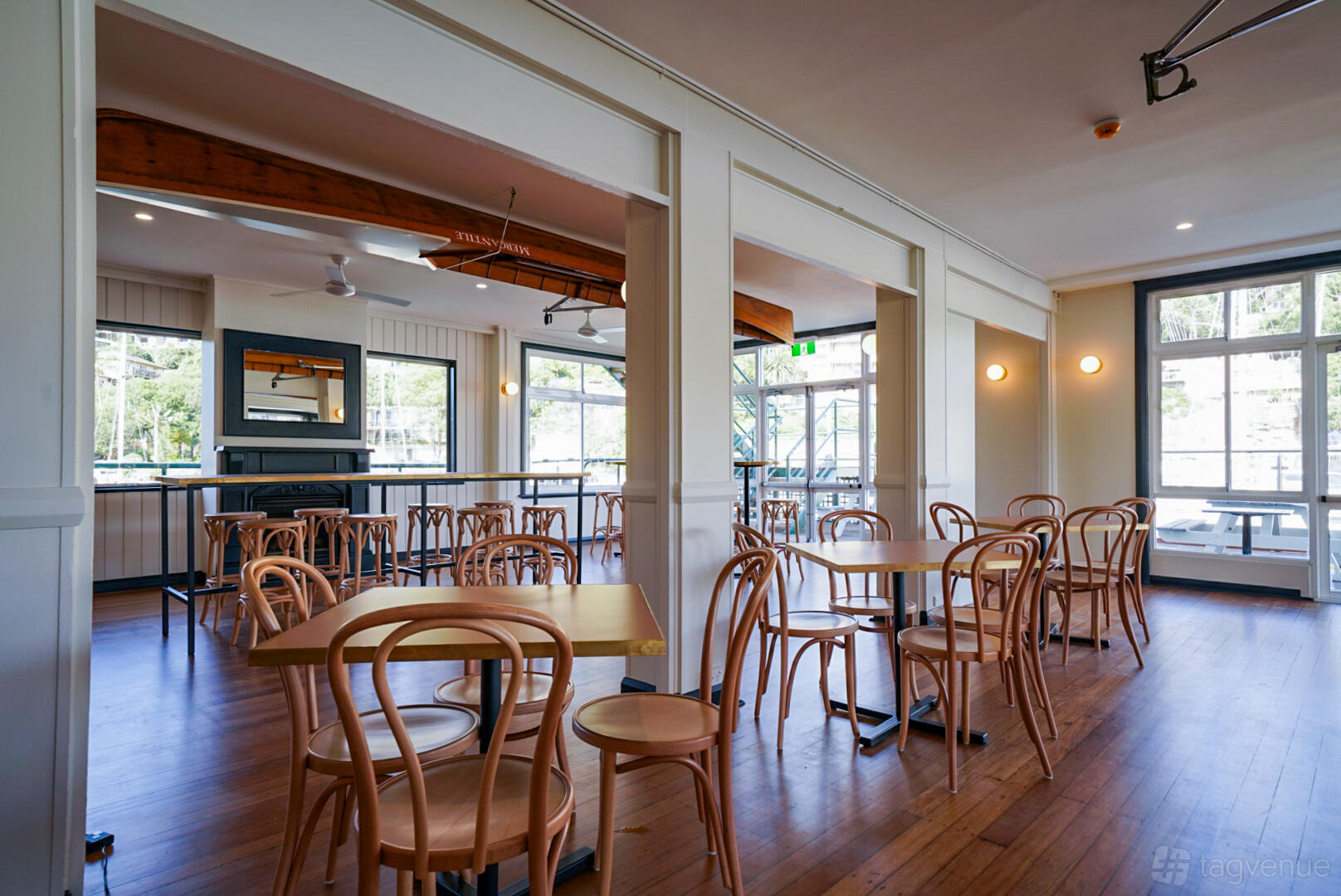 A cafe with wooden chairs, square tables, large windows, and natural light at Archie Bear.
