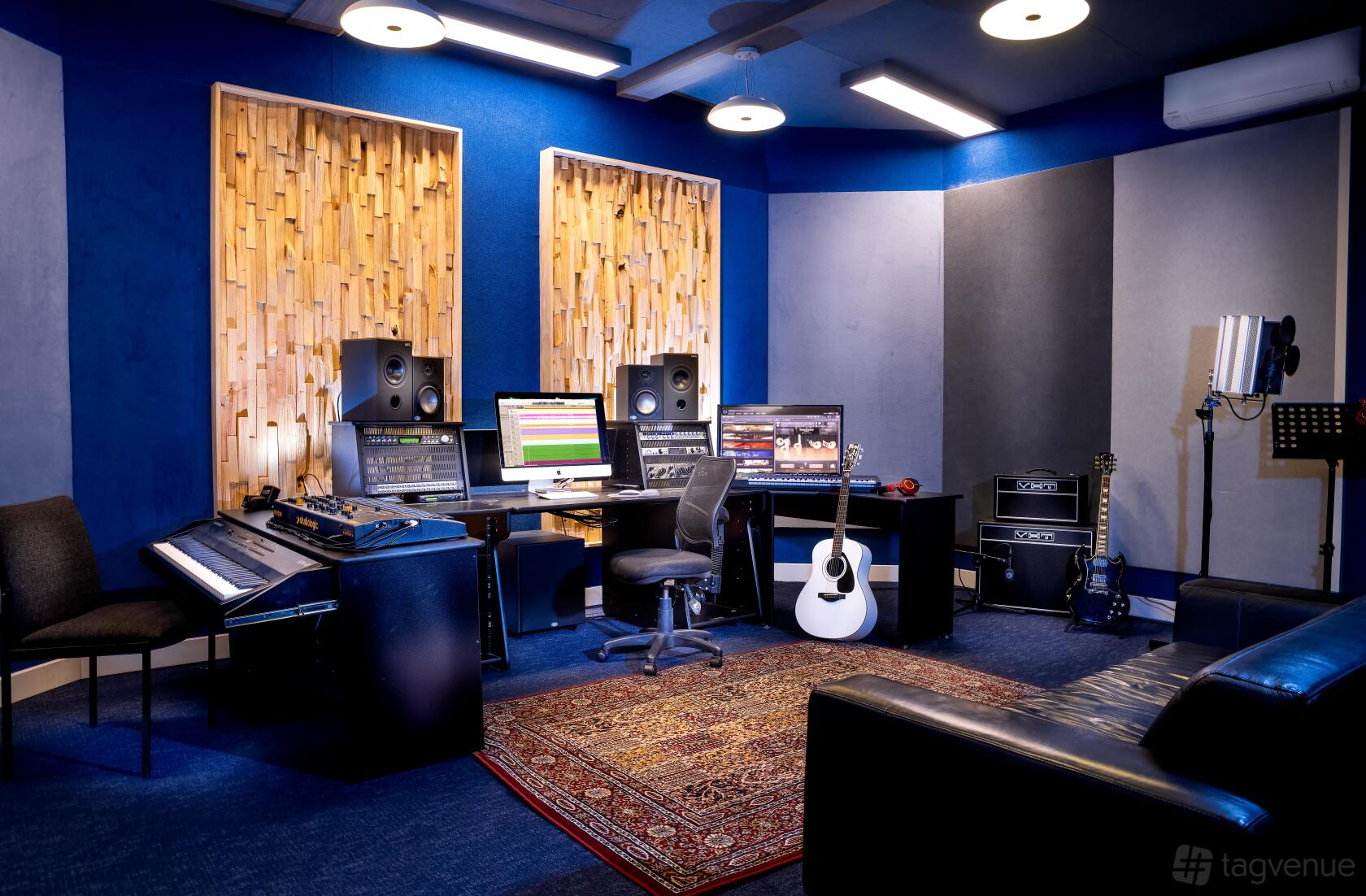 A recording studio with acoustic panels, dual computer monitors, studio monitors, a keyboard, and guitars at Empire Music Studios A.K.A Studio52.