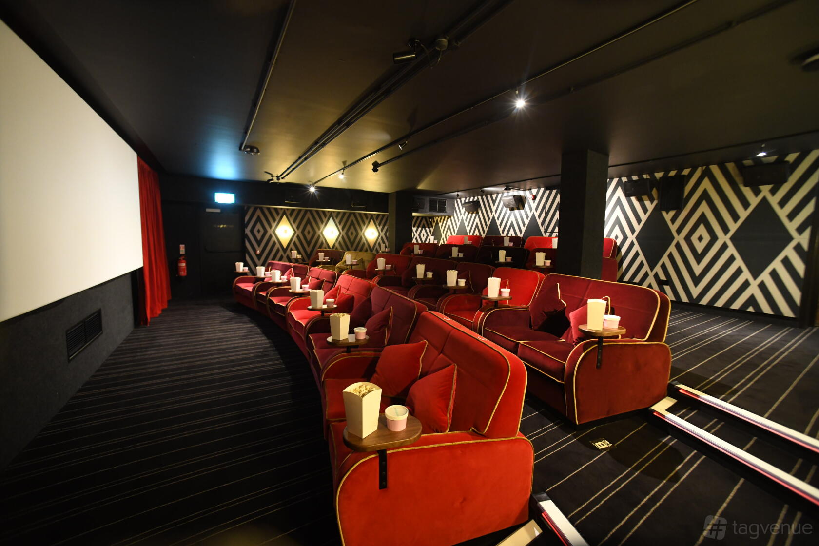 An auditorium with red velvet armchairs, side tables, and geometric wall patterns at Everyman Glasgow