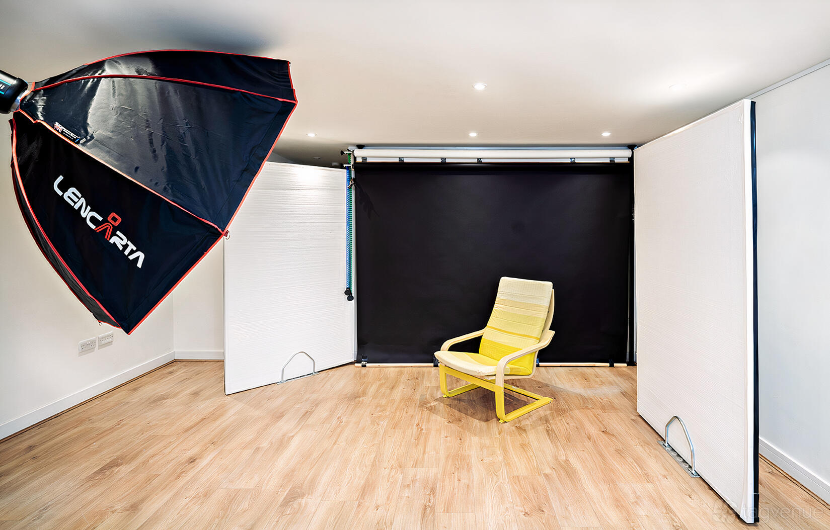 A photo studio with a black backdrop, softbox lighting, and a single yellow chair at Paxton Studio.