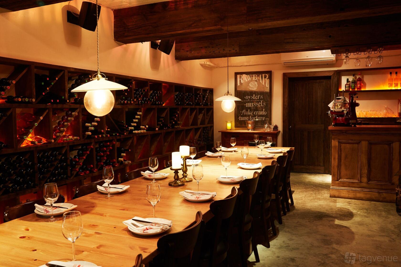 A dining room with a long wooden table, hanging pendant lights, and wall-mounted wine racks at Follia.