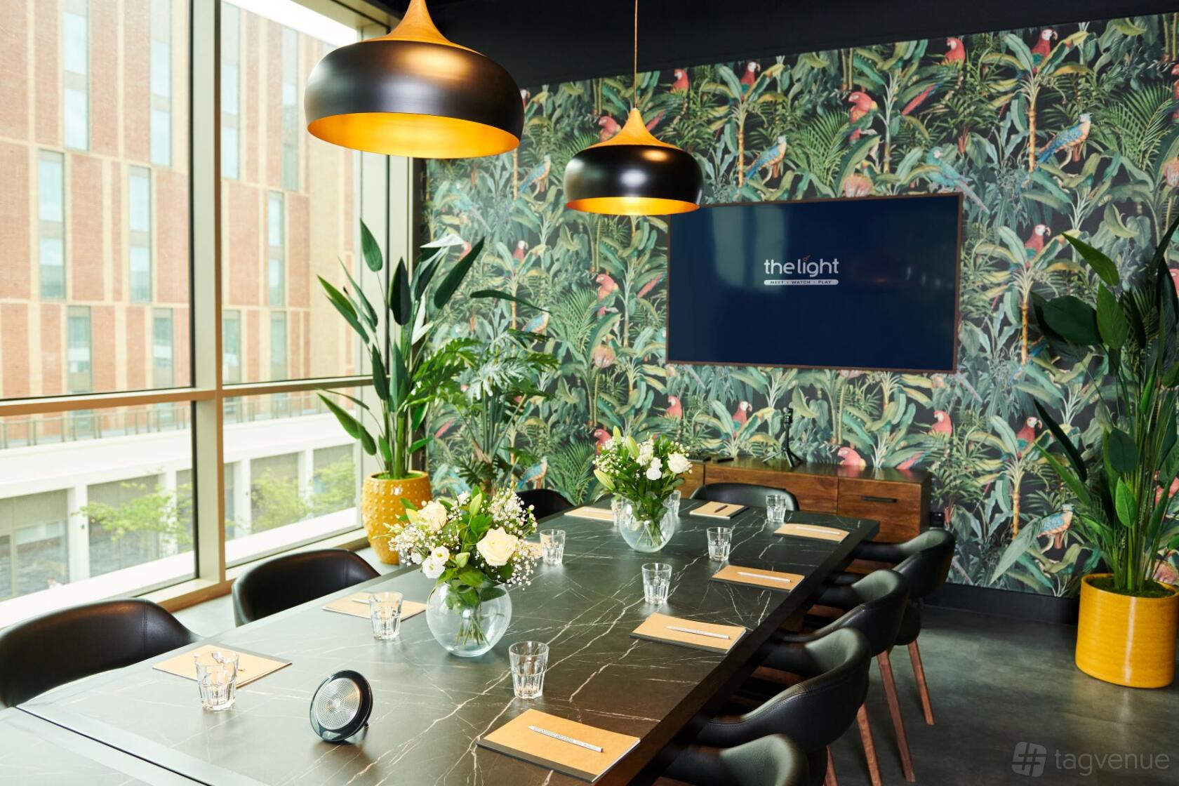 A meeting room with a marble table, pendant lighting, floral arrangements, and a tropical wallpaper at The Light Banbury.