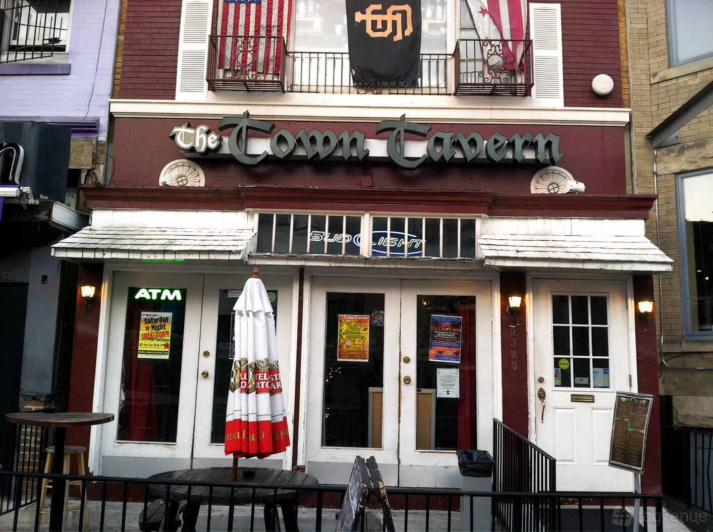 A pub exterior with burgundy facade, large sign, outdoor umbrella, and posters at Town Tavern.