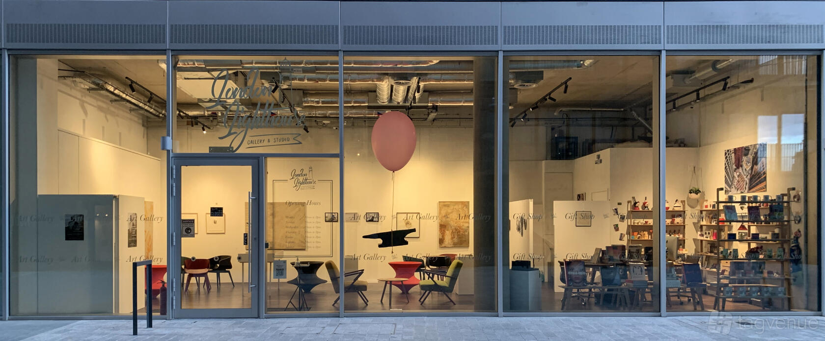 A gallery with floor-to-ceiling windows, exposed ceilings, eclectic seating, and a large pink balloon at London Lighthouse Gallery & Studio.
