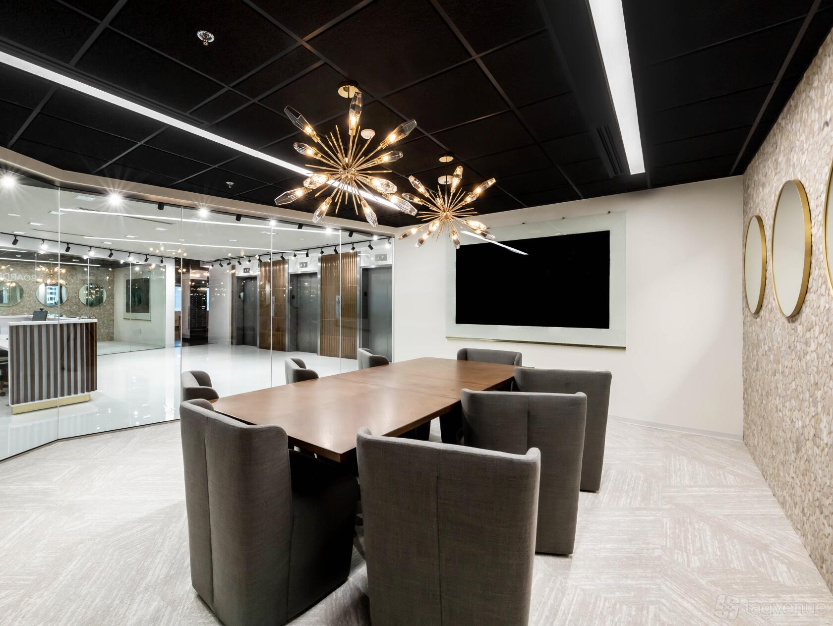 A boardroom with a long wooden table, gray upholstered chairs, and modern pendant lighting at Lucid Private Offices - Buckhead.