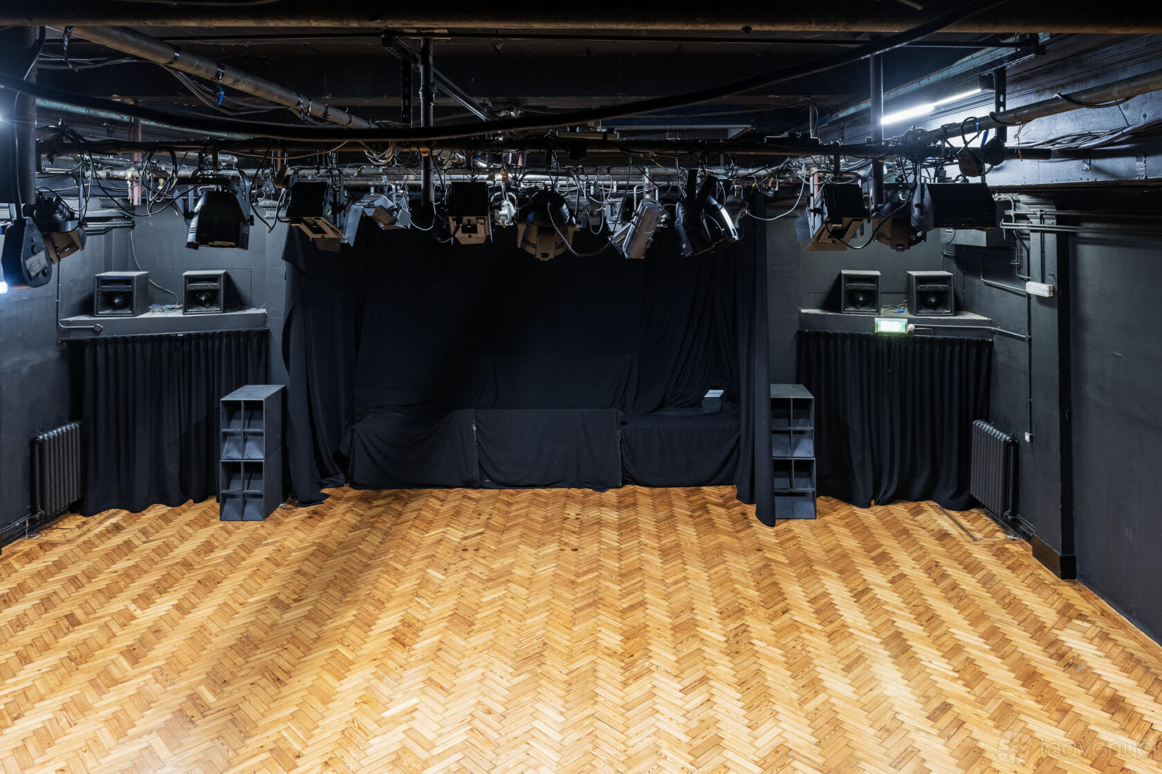 An event venue with a parquet wooden floor, black stage curtains, and overhead stage lighting at Chats Palace.