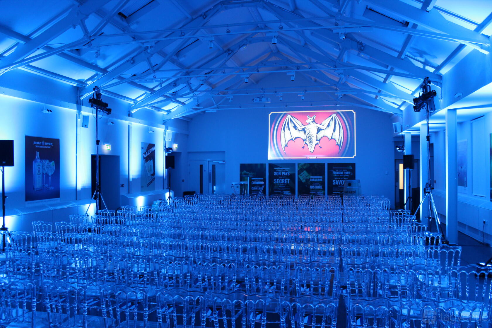 A hall with rows of clear chairs, blue ambient lighting, and exposed beams at Bombay Sapphire Distillery