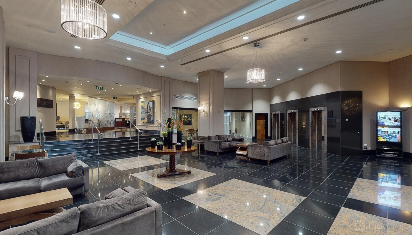 A hotel event space lobby with marble flooring, contemporary chandeliers, and grey lounge seating at Chelsea Harbour Hotel & Spa.