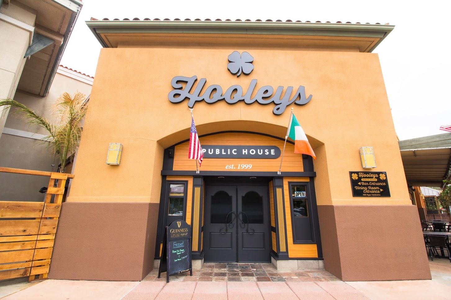 A restaurant entrance with double doors, Irish and American flags, and large Hooleys signage at Hooleys Public House- Rancho San Diego.