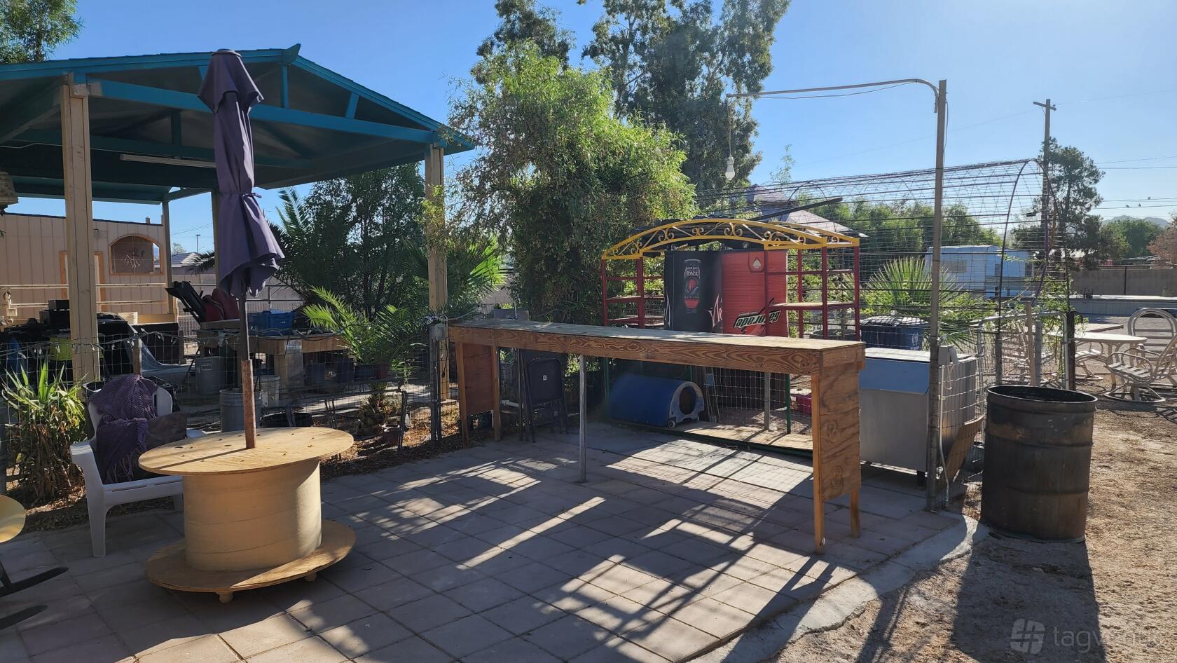 An outdoor hotel space with a wooden bar table, patio umbrella, and shaded seating at Ranch Style Backyard.