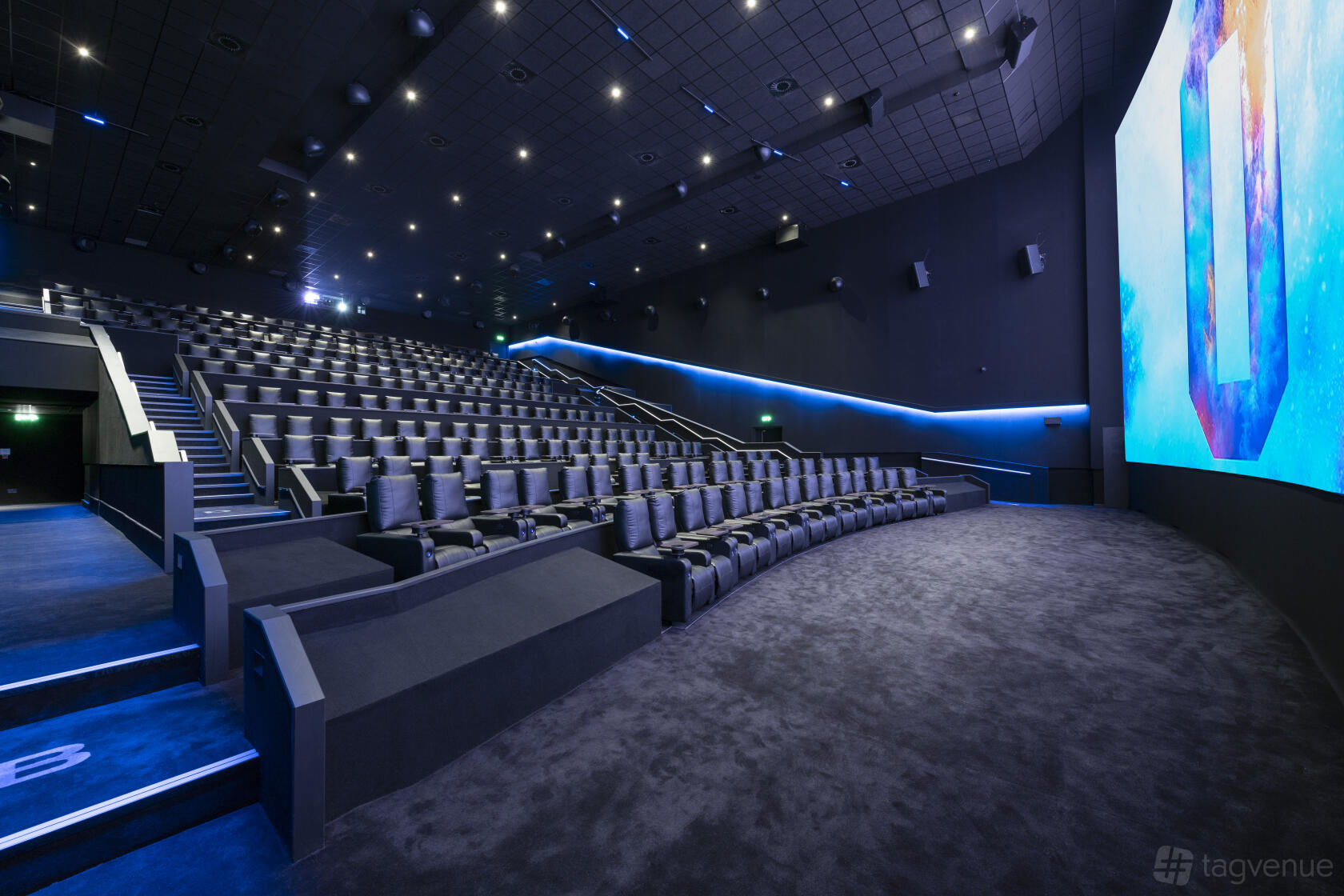 A cinema auditorium with tiered plush seating, blue accent lighting, and a large digital screen at ODEON LUXE Birmingham Broadway Plaza.