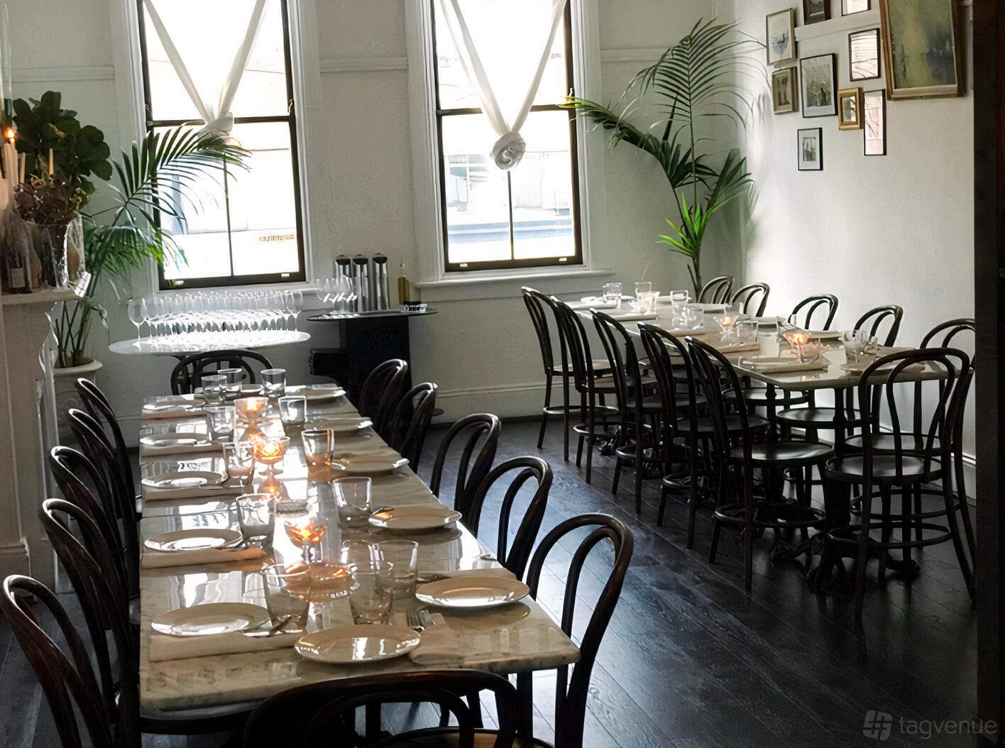 A restaurant dining room with marble tables, dark bentwood chairs, candles, and large windows at Osteria di Russo & Russo.