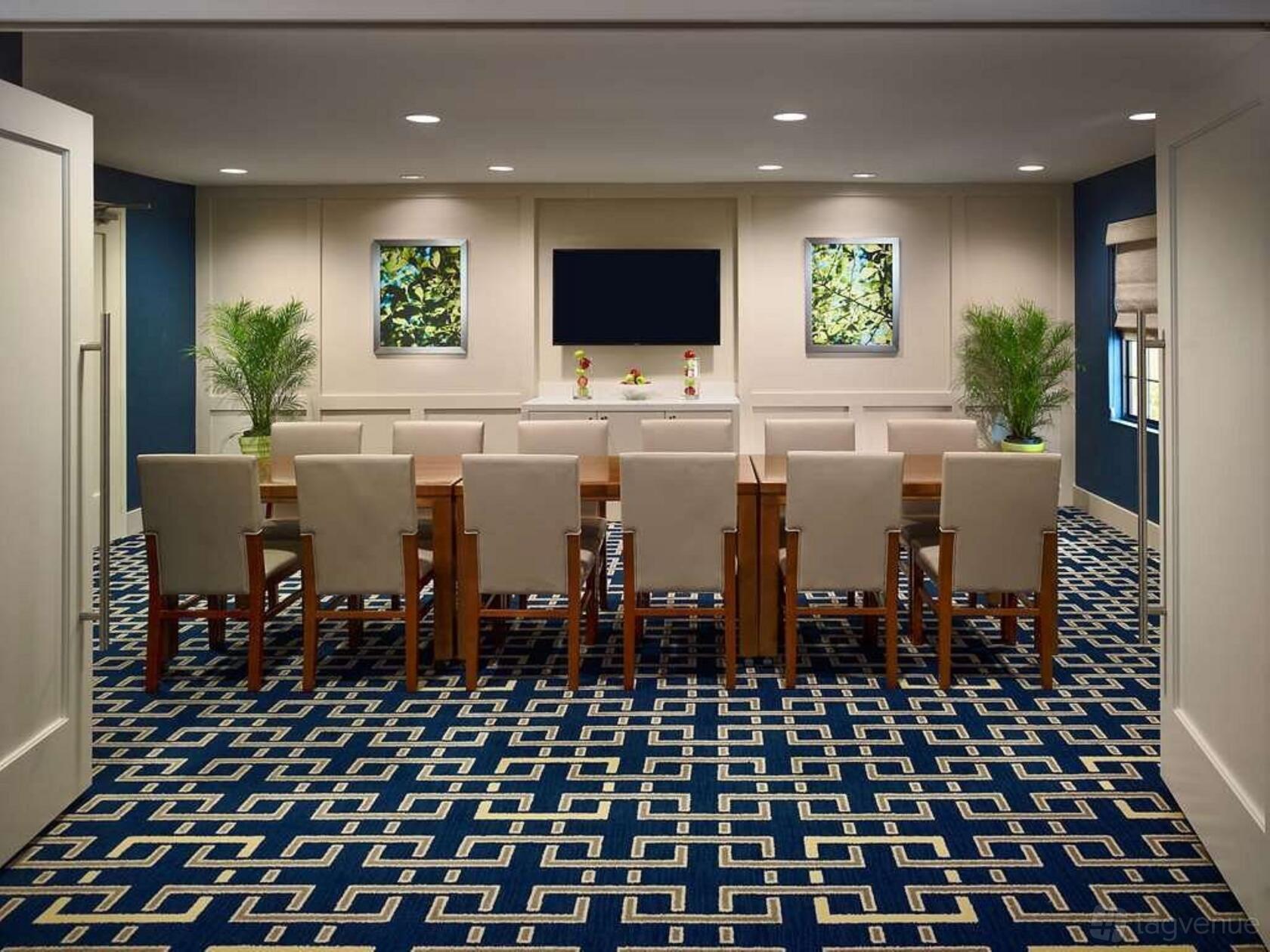 A meeting room with a long wooden table, cream chairs, framed artwork, and patterned carpet at Sonesta.