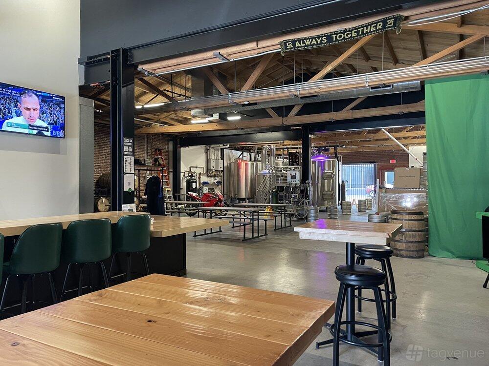 A brewery tasting room with wooden tables, metal brewing tanks, and exposed beams at HiDef Brewing Co.