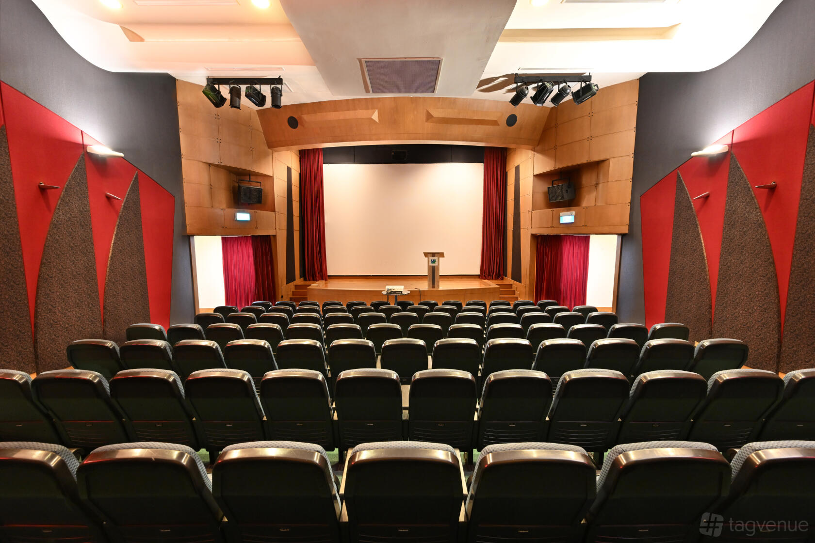 An event venue with tiered theater seating facing a stage with a podium and projector screen at Seletar Country Club.