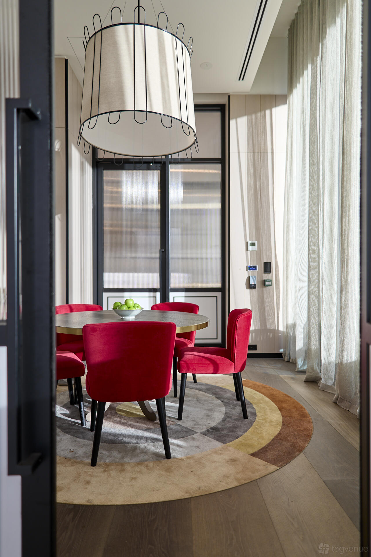A hotel dining room with a round table, red upholstered chairs, and a bowl of green apples at Dorsett Melbourne.