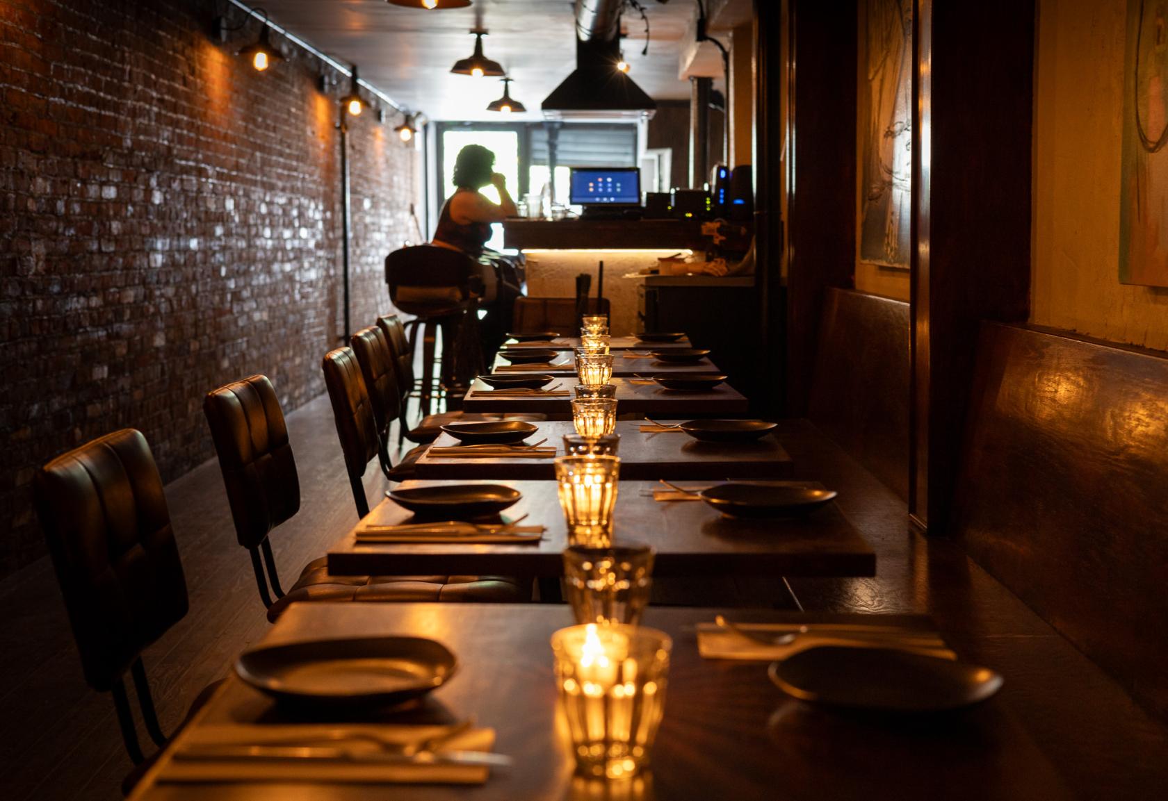 A bar with exposed brick walls, warm ambient lighting, and long wooden tables set with candles at Nine Cases.
