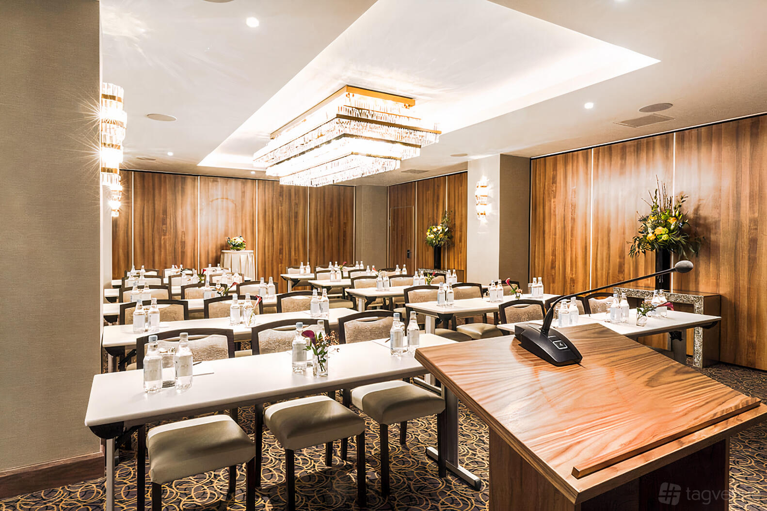 An event space with crystal chandeliers, wood panel walls, and rows of tables with bottled water at The Royal London Suites.